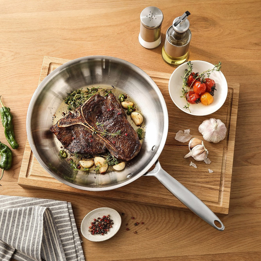 T-Bone-Steak mit Knoblauch in einer Bratpfanne aus 3-Ply Edelstahl auf einem Schneidebrett