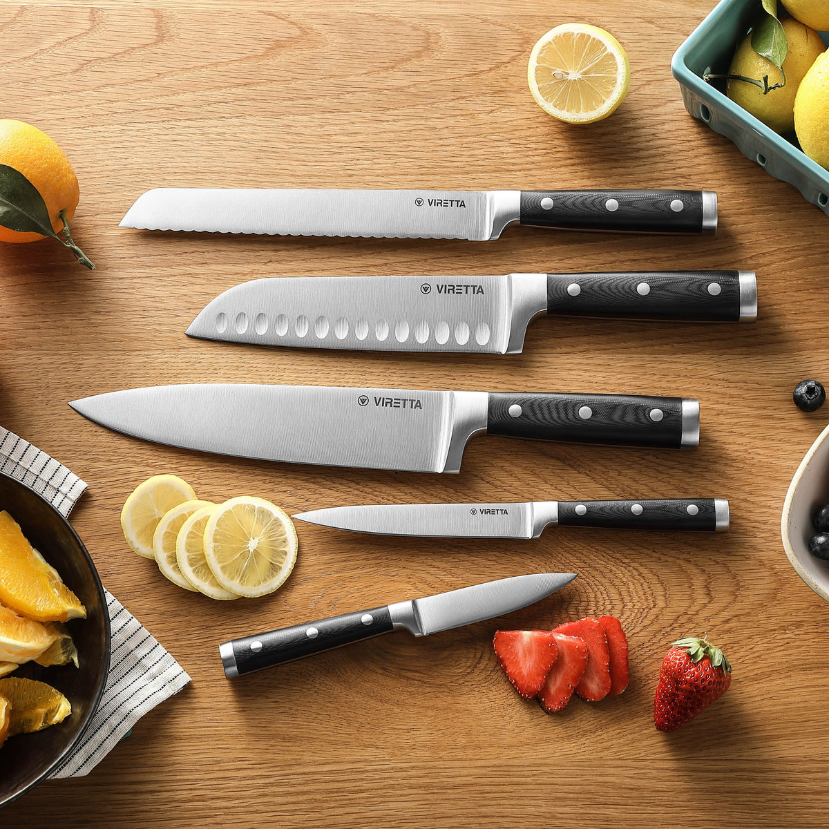 Alle fünf Classic-Messer auf einem Holztisch mit Zitronen und Erdbeeren – das Gemüsemesser ganz unten