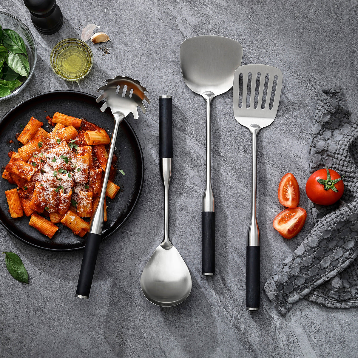 Servierlöffel, Pastalöffel und Pfannenwender mit Griffen aus G-10 neben einem Teller Rigatoni mit Tomatensoße