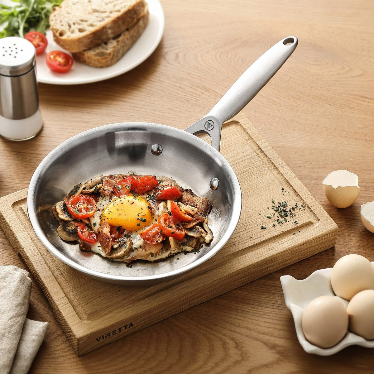 Spiegelei mit Tomaten und Pilzen in einer Bratpfanne aus 3-Ply Edelstahl auf einem Schneidebrett