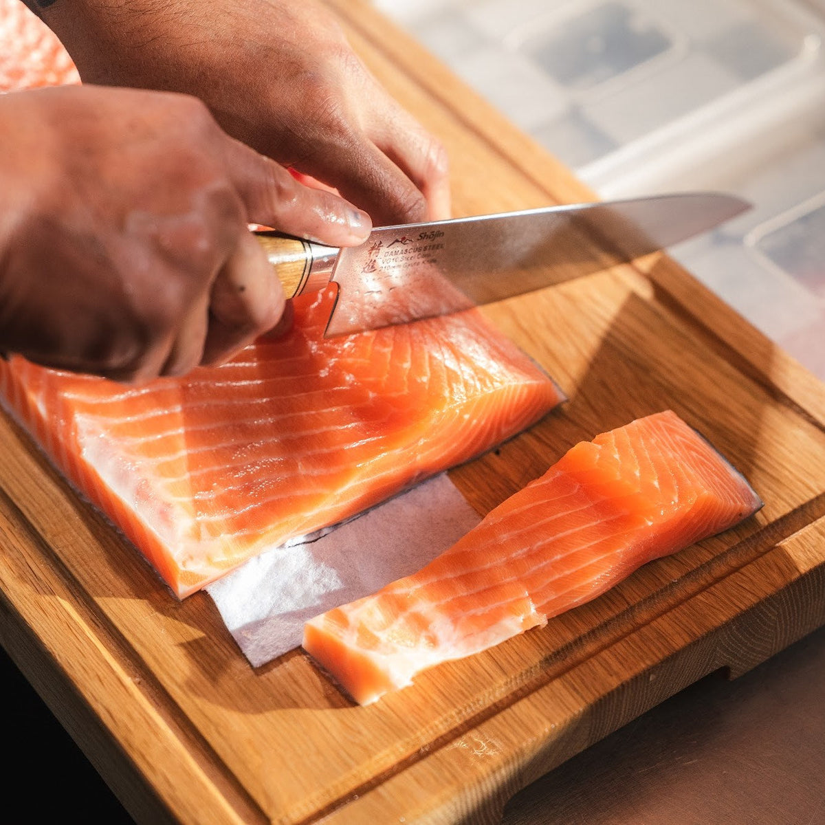 Lachs wird mit einem Shōjin Kaku Gyuto-Kochmesser mit Eichengriff auf einem Schneidebrett aus Eiche portioniert