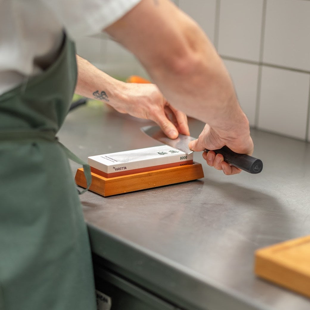 Der Bambushalter mit dem Shōjin Schleifstein 3000/8000, während in einer Restaurantküche ein Messer geschliffen wird