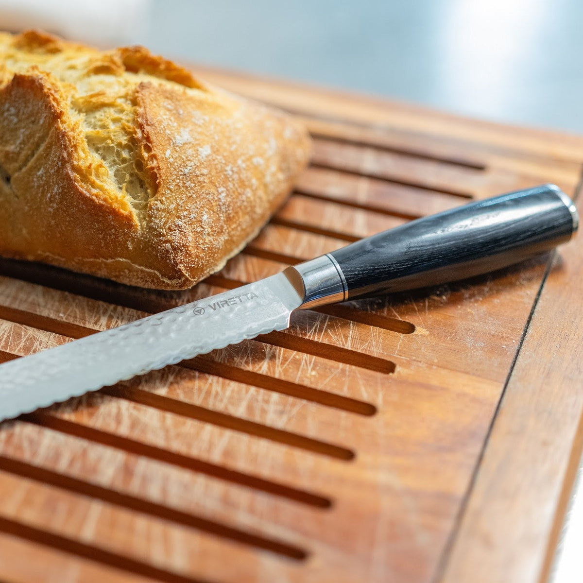 Shōjin Taru Brotmesser mit gehämmerter Klinge neben einem Sauerteigbrot auf einem Brotbrett