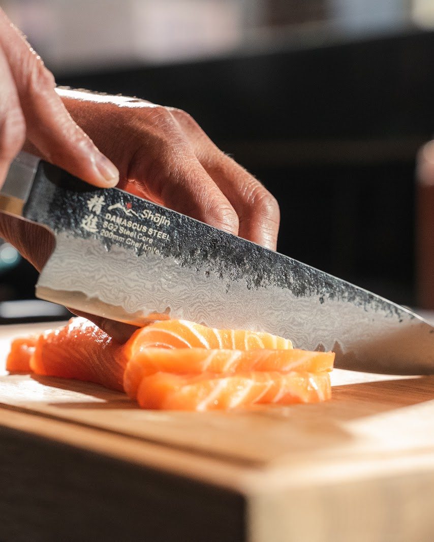 Ein Messer mit gehämmerter Klinge schneidet Lachs auf einem Schneidebrett in Scheiben