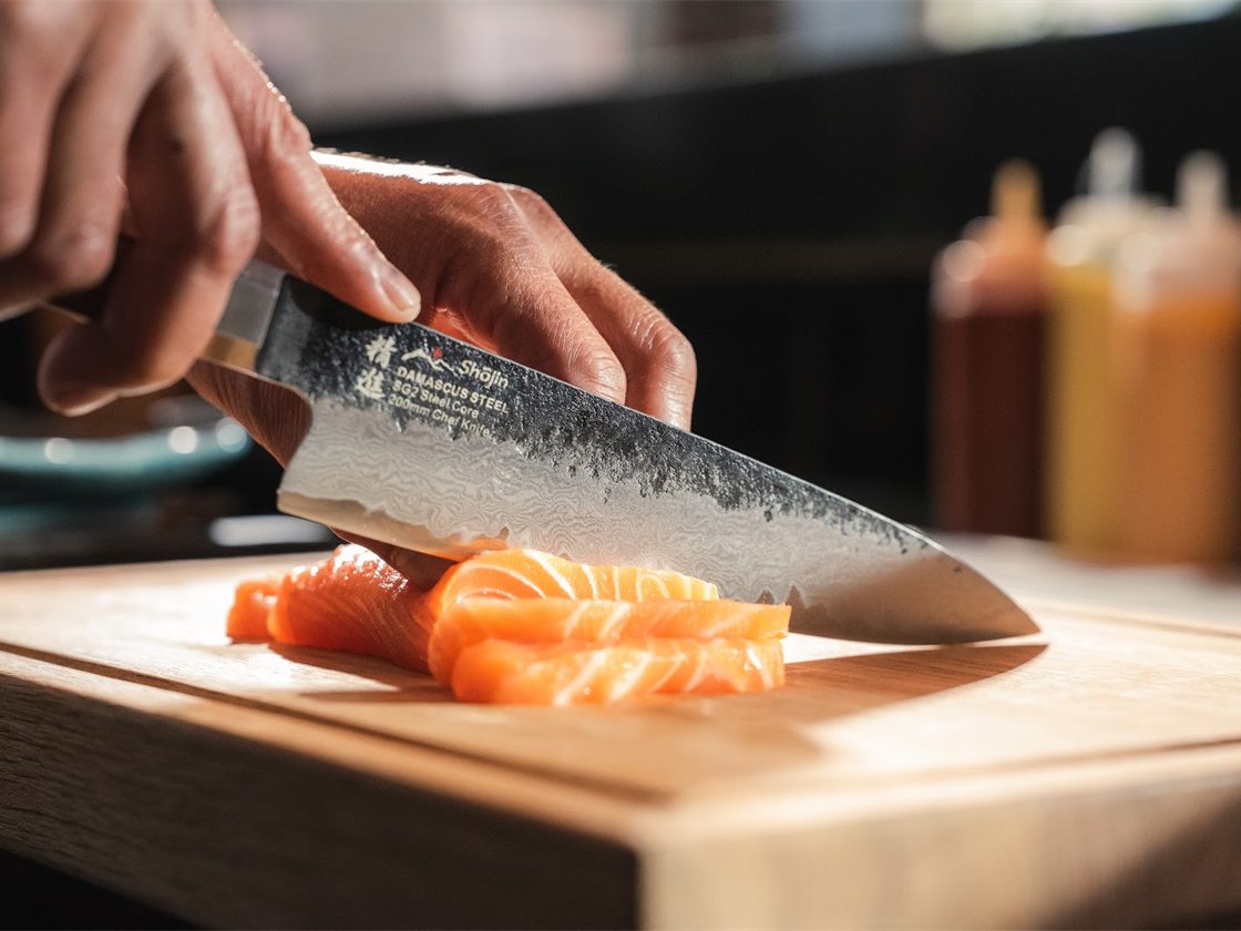 Ein Messer mit gehämmerter Klinge schneidet Lachs auf einem Schneidebrett in Scheiben